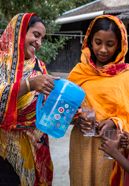 Khaleda Begum (l.), profitiert von ihrer Regenwassergewinnung, die von CCDB gestellt wurde und kann jetzt ihren Kindern Muranahar Begum (m.) und Sohn Shojib Begum sauberes Trinkwasser aus dem Wassertank zapfen. Die Menschen in den kleinen Siedlungen an den Fluessen in der Naehe von Shyamnagar in Sued Bangladesch, spuehren deutlich den Klimawandel. Der Meeresspiegel steigt und Daemme werden zerstört. Da durch werden Felder und die wichtigen Suesswasserteiche ueberflutet und versalzen. CCDB Bangladesch arbeitet an Suesswassergewinnungs-Projekten und sorgt dafuer, dass die Menschen nach und nach sauberes Trinkwasser erhalten. CCDB Bangladesch